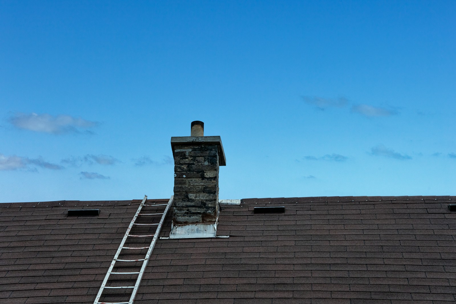 A tiled house roof with chimney and ladder; roof condition context.